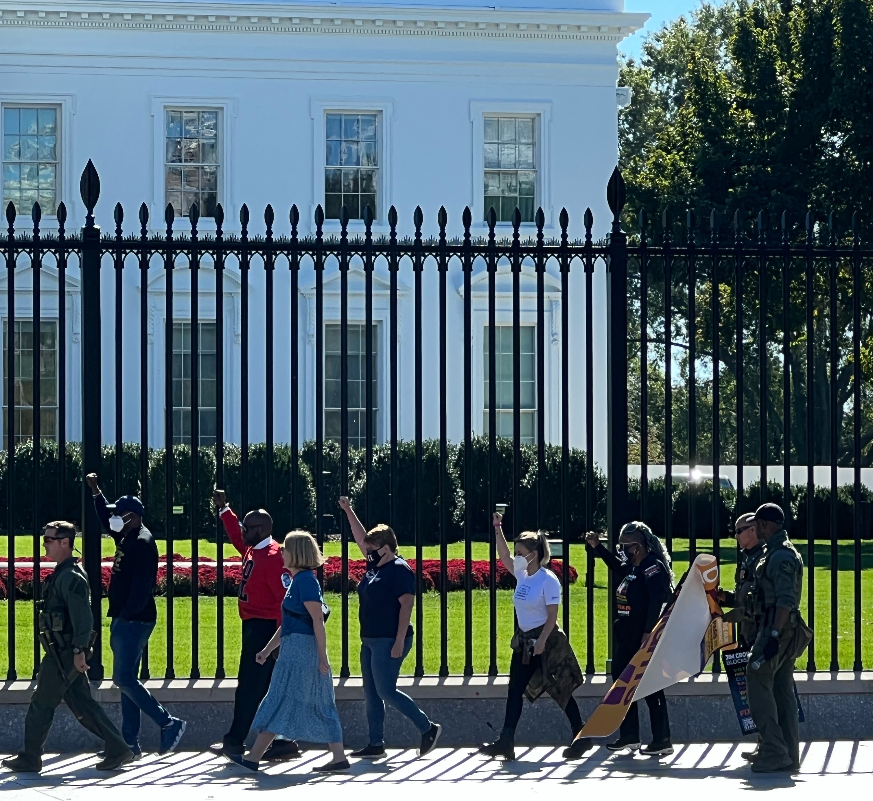 Protestors walking in a line in front of the White House with their fists up; Polic officer ushering them forward for arrest